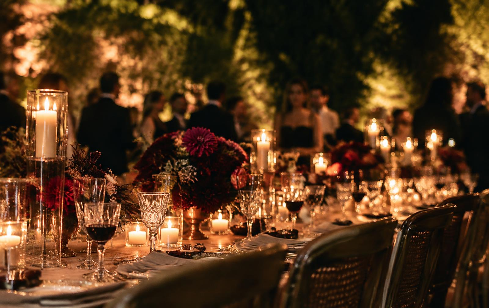 A candlelit dinner table set with red wine and flowers